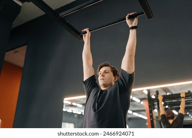 Exhausted muscular male hanging on bar and does one pull-up during sport workout training in modern gym. Tired motivated beginner sportsman showing hard expression on face in pulling up own body. - Powered by Shutterstock