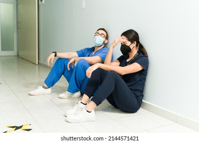 Exhausted Nurse And Doctor With Face Masks Resting In The Hospital Aisle. Medical Staff Feeling Tired 