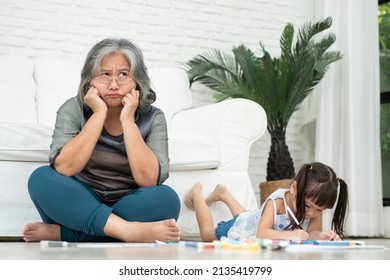 Exhausted Old Elderly Grandmother Sit On Floor In Living Room And Feel Unwell Tired From Little Children Running And Playing Loud, Suffer From Headache, Female Nanny Feels Exhausted By Noisy Kids