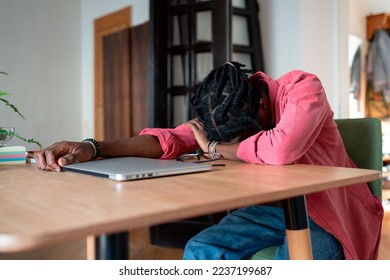 Exhausted overloaded African guy remote worker sleeping on desk while working remotely from home, suffering from freelancer burnout. Student guy experiencing sleep deprivation from virtual learning