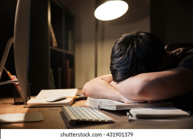 Exhausted Overworked Young Man Studying And Sleeping On The Table In Dark Room At Home