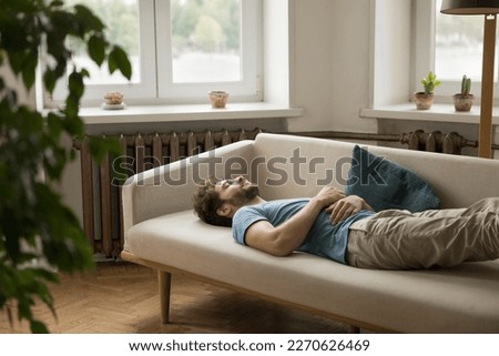 Exhausted peaceful sleepy young woman lying on back on couch with hand on belly, sleeping, resting on sofa at daytime, taking break, pause, feeling fatigue after insomnia