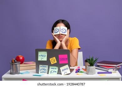 Exhausted Person. Portrait Of Overworked Young Woman Sitting At Desk With Stickers On Eyes And Using Laptop, Doing Tiresome Tasks, Isolated Over Purple Studio Background. Stress And Deadlines