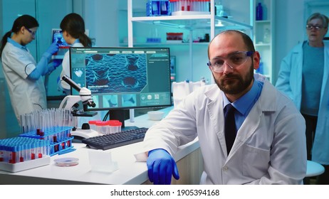 Exhausted Portrait Of Chemist Doctor Looking Up At Video Camera Sitting In Equipped Lab Working Late At Night. Examining Virus Evolution Using High Tech And Chemistry Tools For Vaccine Development.