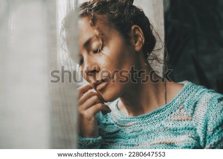 Exhausted and sad woman alone at home near the window with closed eyes and depressed expression on face. Closeup portrait of adult female people with sadness. People and mental burnout problems life