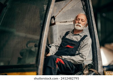 An exhausted senior blue collar worker is sleeping in forklift. - Powered by Shutterstock