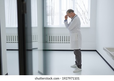 Exhausted senior doctor in medical uniform.Coronavirus Covid-19 outbreak.Mental stress of medical worker. Overworked healthcare professional. side view - Powered by Shutterstock