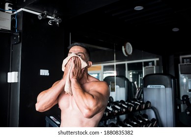 An Exhausted Shirtless Asian Man Wipes His Sweaty Face With A Hand Towel After A Intense Gym Workout. Gym Or Fitness Club Setting.