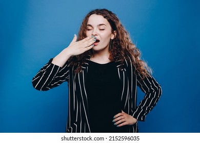 Exhausted sleepless woman has curly hair yawns covers mouth in wants to sleep awakes very early isolated over blue background. People sleeping disorders concept - Shutterstock ID 2152596035