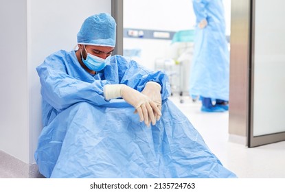 Exhausted Surgeon Or Nurse In Protective Clothing Sits Burned Out In Front Of The Operating Room