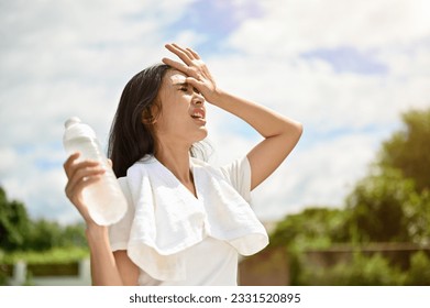 An exhausted and sweaty young Asian woman in sportswear is fighting the heat wave while running in a park on a sunny summer day. summer activity, heat stroke, dehydrated - Shutterstock ID 2331520895
