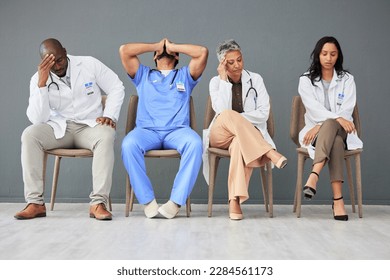 Exhausted, tired and doctors waiting in the hospital with frustration, sad and burnout. Upset, professional and team of healthcare workers sitting in a line in a hallway for meeting in medical clinic - Powered by Shutterstock