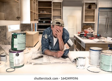 Exhausted, Tired, Frustrated, House Painter In Messy Painters Clothes, Face In Hands, Holding Wet Paintbrush In Fixer Upper Home Kitchen Remodel, Dripping Paint Cans On Counter, Cabinet Doors Off