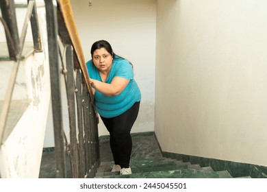 Exhausted tired overweight indian woman have difficulty climbing stairs, breathing gasping, take resting,  fitness healthcare, female obesity. Loose weight, burn fat, plus size lady fatigue. Knee pain