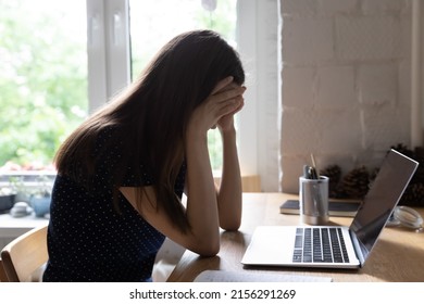 Exhausted upset young student girl sitting at table with laptop, leaning head on hand, suffering from headache, feeling depressed, unhappy, tired, getting bad news. Professional burnout concept - Shutterstock ID 2156291269