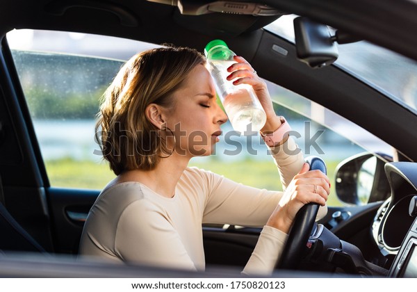 Exhausted woman driver\
feeling headache, sitting inside her car, applies a bottle of water\
to his forehead, hot weather. Stop after driving car in traffic\
jam. Blood pressure