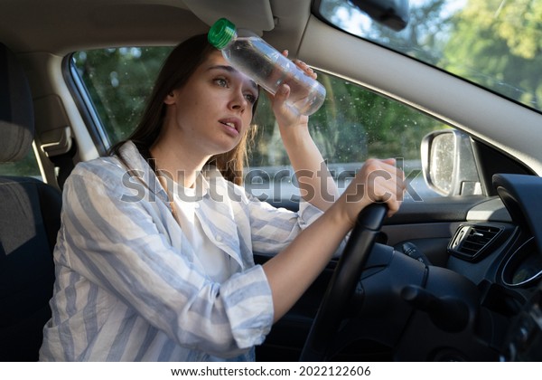 Exhausted woman driver feeling headache, sitting inside\
her car, applies bottle of water to forehead, hot weather. Tired\
girl stop after driving car in traffic jam. Blood pressure, heat\
concept. 
