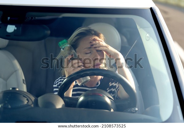 Exhausted woman driver feeling headache, sitting\
inside her car, applies bottle of water to forehead, hot weather.\
Tired female stop after driving car in traffic jam. Blood pressure,\
heat concept.