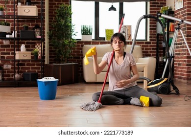 Exhausted Woman Eating A Snack While Doing Deep Spring Cleaning In Urban Apartment, Sitting On The Floor Taking A Short Break. Keeping Everything Clean And Tidy At Home, House Chores.