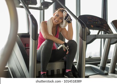 Exhausted woman at the gym wiping off sweat while smiling - Powered by Shutterstock