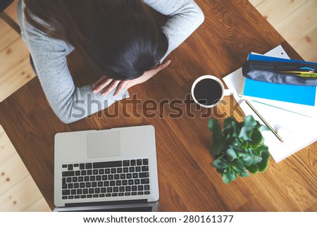 Exhausted  woman sitting at table in home office with head lying on table.