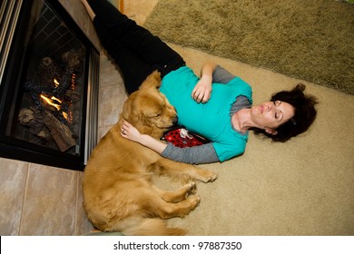 An Exhausted Woman Sleeping Comfortably Next To A Fire With Her Golden Retriever Dog.