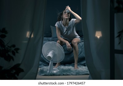Exhausted woman suffering suring the heatwave, she is holding a water bottle and sitting in front of a cooling fan in the bedroom