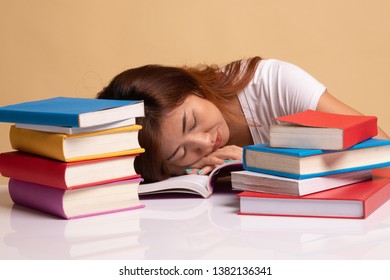 Exhausted Young Asian woman sleep with books on table on beige background