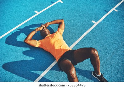 Exhausted young athletic African man in sportswear lying on the lanes of a running track taking a break from training
