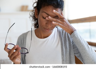 Exhausted Young Biracial Woman Take Off Glasses Massage Eyes Suffer From Blurry Vision Or Dizziness, Tired African American Female Struggle With Headache Or Migraine, Health Problem Concept