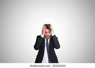 Exhausted young business man with dark eye bags, on gray background.
