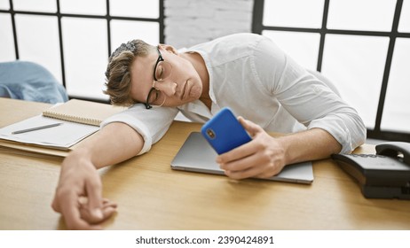 Exhausted young caucasian businessman, smartphone in hand, loses battle with stressâ€“ nobly crashes asleep on office table, job tedium takes its toll. - Powered by Shutterstock