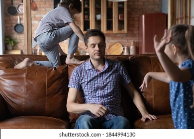 Exhausted Young Caucasian Father Sit On Sofa At Home Distressed By Ill-behaved Active Kids Playing. Unhappy Upset Dad Feel Tired Stressed With Naughty Disobedient Loud Children. Upbringing Concept.