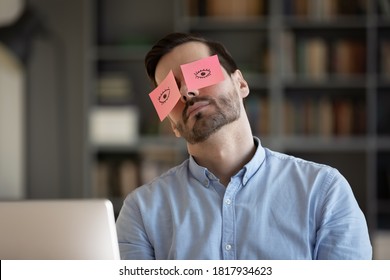 Exhausted young Caucasian man worker have sticker pads on eyes sleeping near computer in office. Tired millennial male employee fall asleep doze off at workplace, feel overwhelmed drained at work.