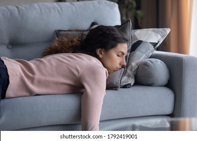Измученная молодая кавказская женщина, лежащая на удобном диване в гостиной, спящая после тяжелого рабочего дня, уставшая тысячелетняя женщина засыпает на диване дома, вздремнет или мечтает, концепция усталости