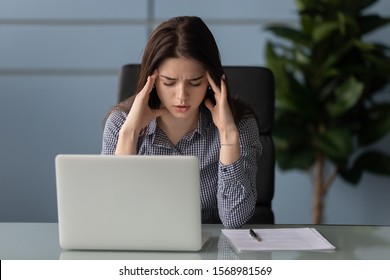 Exhausted young female worker massage touch temples suffer from strong migraine or headache in office, tired millennial woman employee struggle with dizziness have eyesight problems or blurry vision