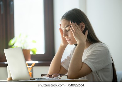 Exhausted young female worker is tired from work. Stress and headache behind laptop on job. Overwork, distress, negative emotions concept