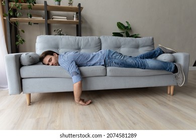 Exhausted young man fell asleep on comfortable couch in modern living room, having no energy after hard working day. Tired depressed unmotivated caucasian guy napping on sofa at home, fatigue concept. - Shutterstock ID 2074581289