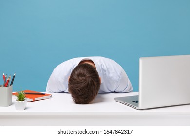 Exhausted young man in light shirt sit, work at desk with pc laptop isolated on pastel blue background. Achievement business career lifestyle concept. Mock up copy space. Laid his head down on desk