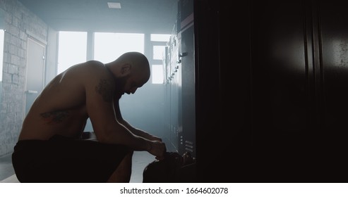Exhausted young shirtless man sitting alone in dark gym locker room feeling sad after failure day. Good fighting spirit. - Powered by Shutterstock