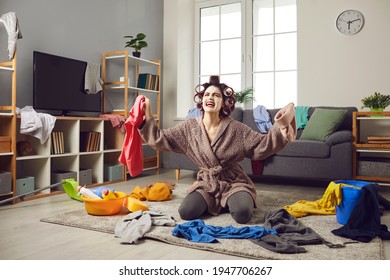 Exhausted Young Woman Cleaning Her House. Desperate Tired Busy Housewife In Hair Curlers And Face Mask Picking Up Scattered Clothes From Floor, Crying And Complaining About Terrible Mess At Home