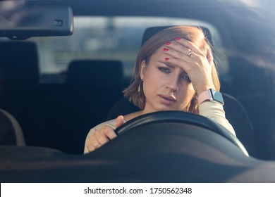Exhausted young woman driver sitting in her car, feeling emotional burnout after work, looking at camera, touching her forehead. Mental health, fatigue.  