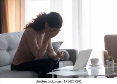 Exhausted young woman dropping off eyeglasses, suffering from dry eyes syndrome, side view. Stressed female freelance worker feeling tired, overwhelmed by huge amount of computer work at home.
