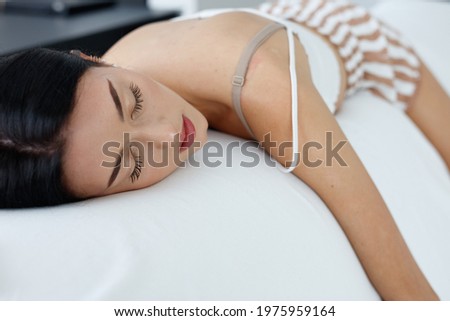 Exhausted young woman enjoying a refreshing sleep with her arm draped over the sofa and a close up on her serene face with closed eyes in a head to toe view