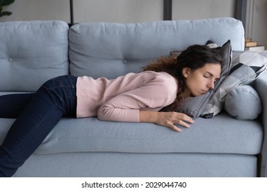 Exhausted young woman lying on sofa sleeping at end of hard workday, after hard-working day. Tired female fall asleep on couch face in cushion. Fatigue relief, no motivation, sleepless night concept