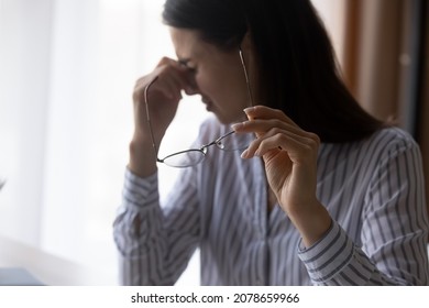 Exhausted Young Woman Taking Off Eyeglasses, Having Blurry Eyesight Or Suffering From Astigmatism Problem. Overwhelmed Millennial Business Lady Massaging Nose Bridge Relieving Pain, Feeling Tired.