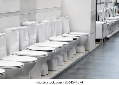 Exhibition of samples of white toilet bowls standing in a row in the warehouse of a plumbing store. Samples of modern sanitary ware for the toilet. New modern toilet in the plumbing store