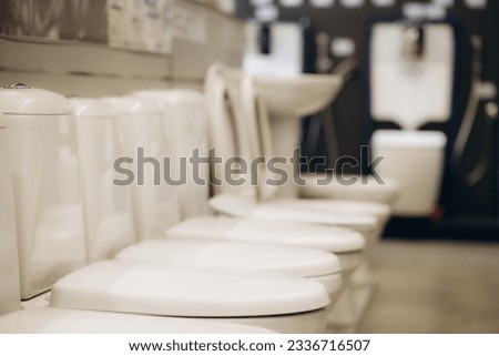 Exhibition of samples of white toilet bowls standing in a row in the warehouse of a plumbing store. Samples of modern sanitary ware for the toilet. New modern toilet in the plumbing store.