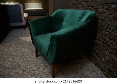 An Exhibition Of A Stylish Comfortable Green Velour Armchair Displayed For Sale, Against Loft Brick Wall Background In A Furniture Design Showroom. Upholstered Furniture Store, Home Design Concept
