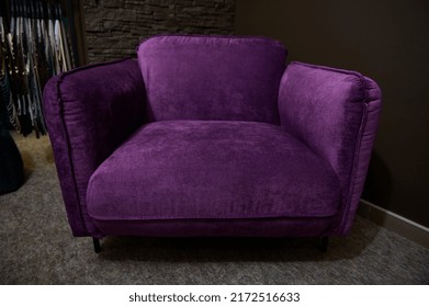 An Exhibition Of A Stylish Comfortable Purple Velour Armchair Displayed For Sale, Against Loft Brick Wall Background In A Furniture Design Showroom. Upholstered Furniture Store, Home Design Concept